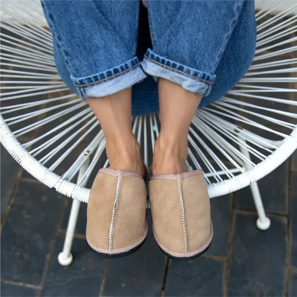 Kalahari Classic sheepskin slippers worn by a person sitting on a white woven chair outdoors.