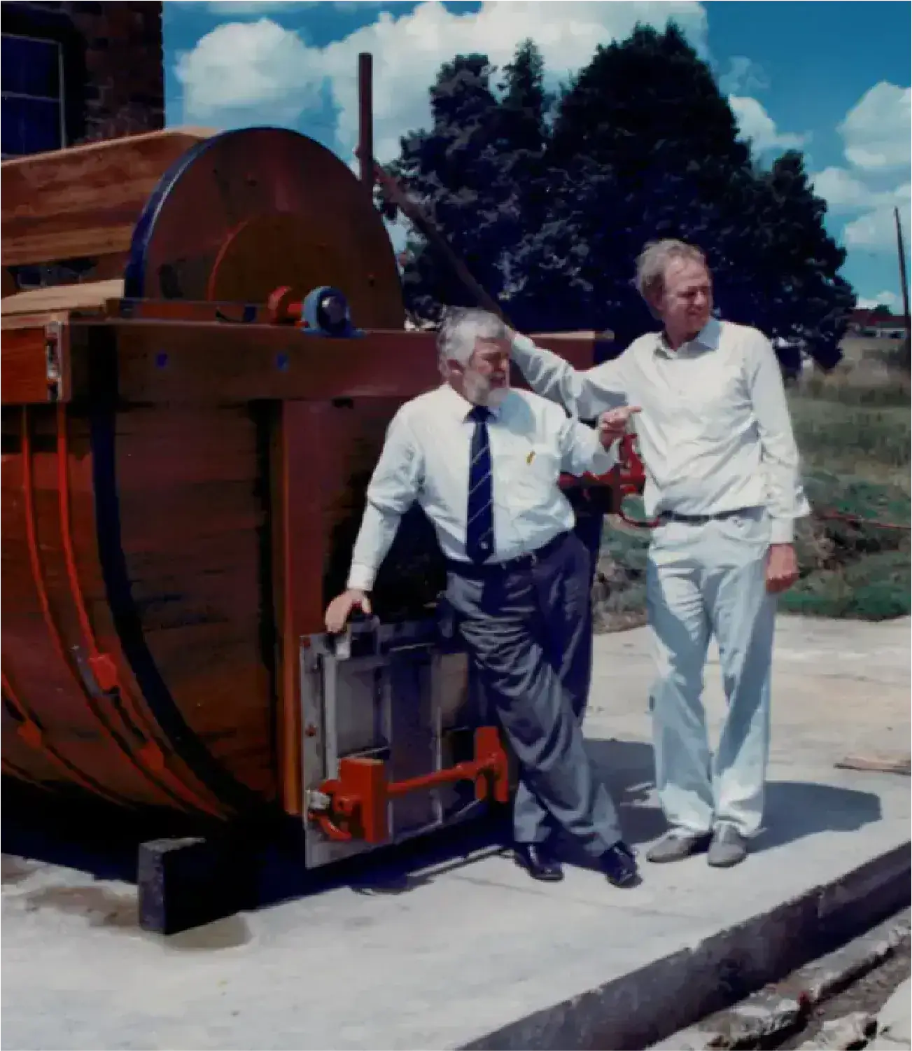 Two men standing beside a large leather tanning drum, symbolizing early craftsmanship at JCP.