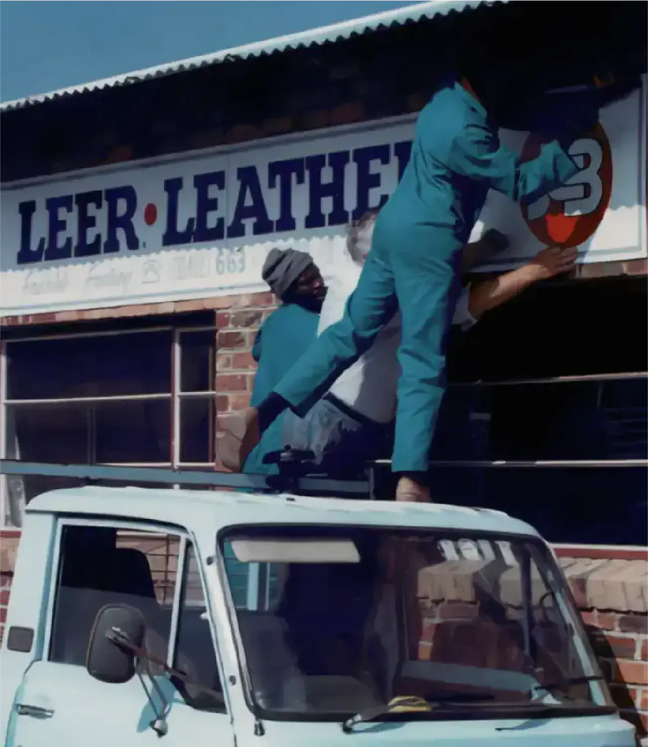 Workers installing the JCB Leathers sign above the storefront using a ladder and a bakkie.