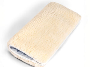Folded sheepskin wheelchair cushion with a soft wool surface and white fabric base.