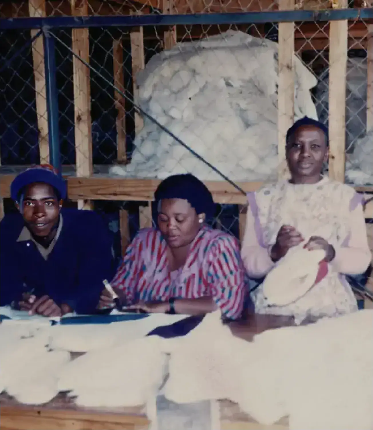 Three women processing and recording sheepskin items inside a sorting and storage facility.